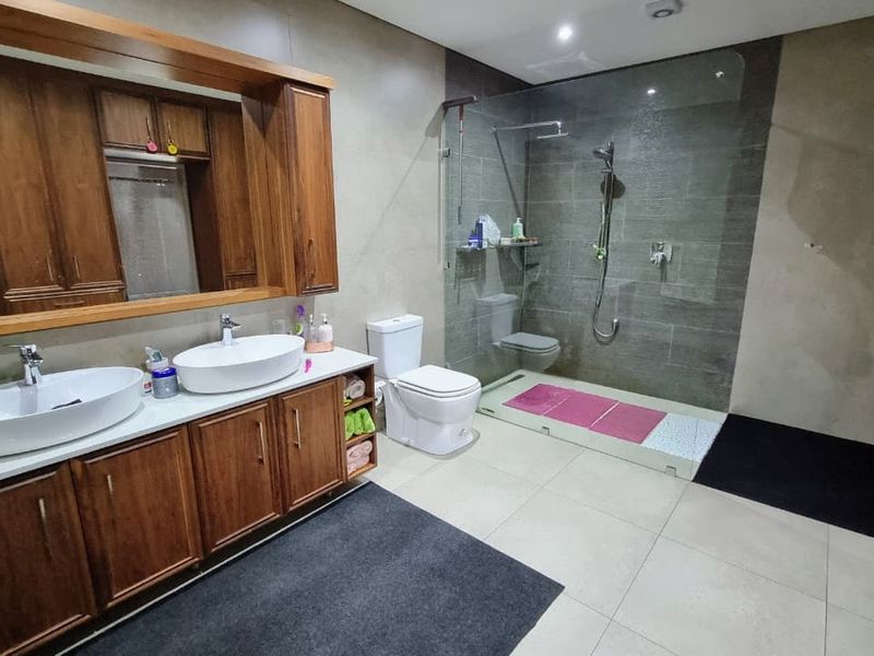 Spacious modern bathroom featuring a double vanity with wooden cabinetry, a large frameless glass walk-in shower, and neutral floor-to-ceiling tiling.