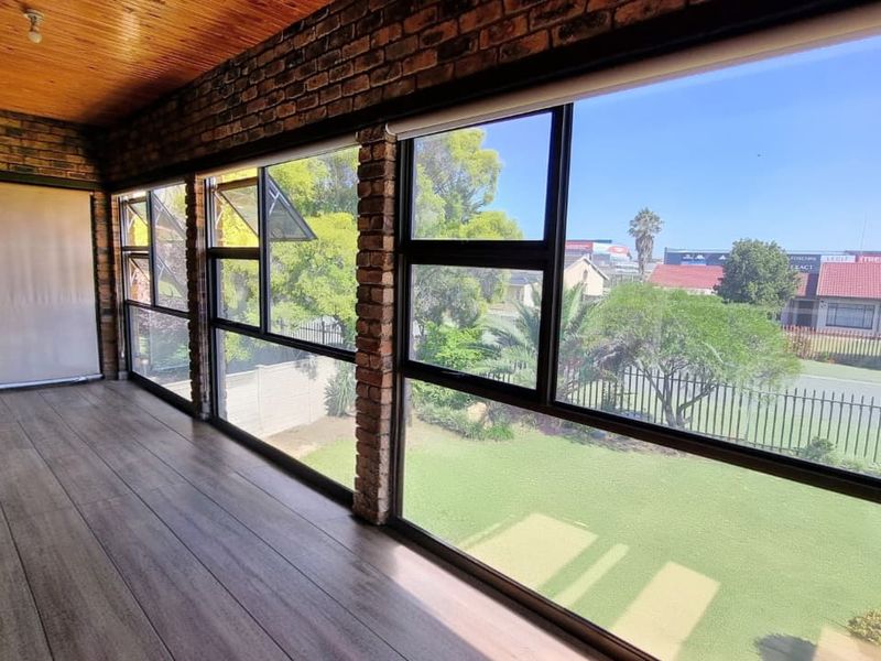 A sunroom or enclosed patio featuring exposed brick walls, timber-look flooring, a wood-paneled ceiling, and large windows overlooking the front garden.