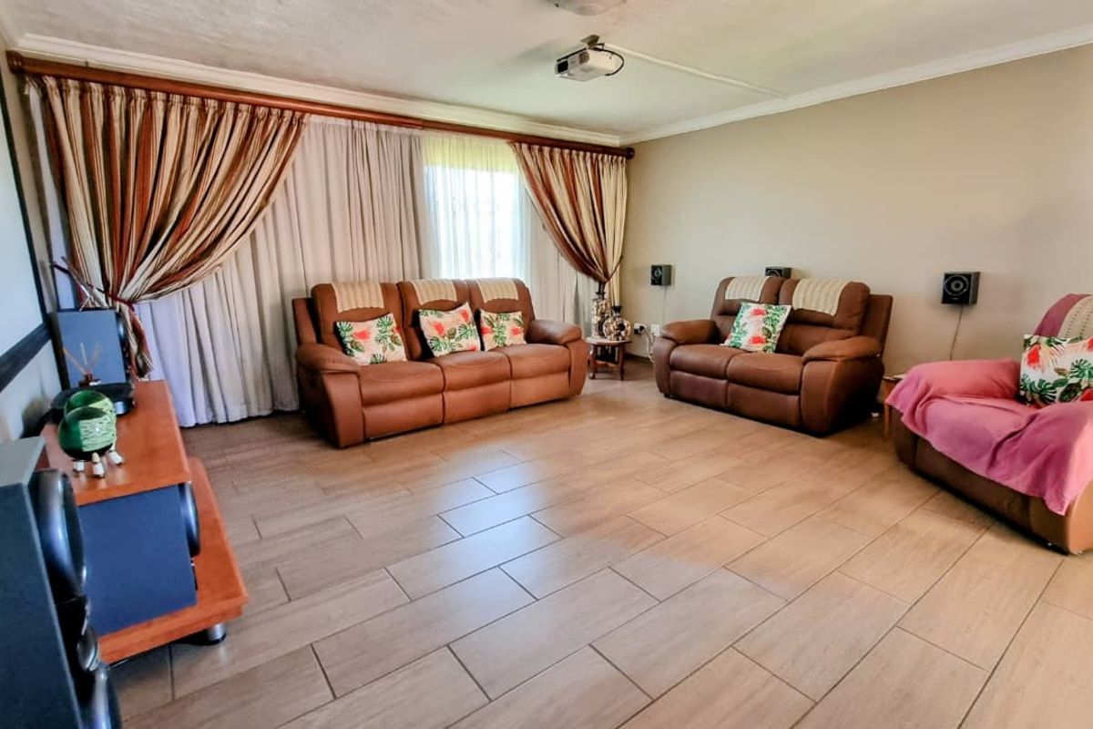 Spacious living room featuring large windows with floor-to-ceiling curtains, tiled flooring, and a ceiling-mounted projector, ideal for a home cinema setup.