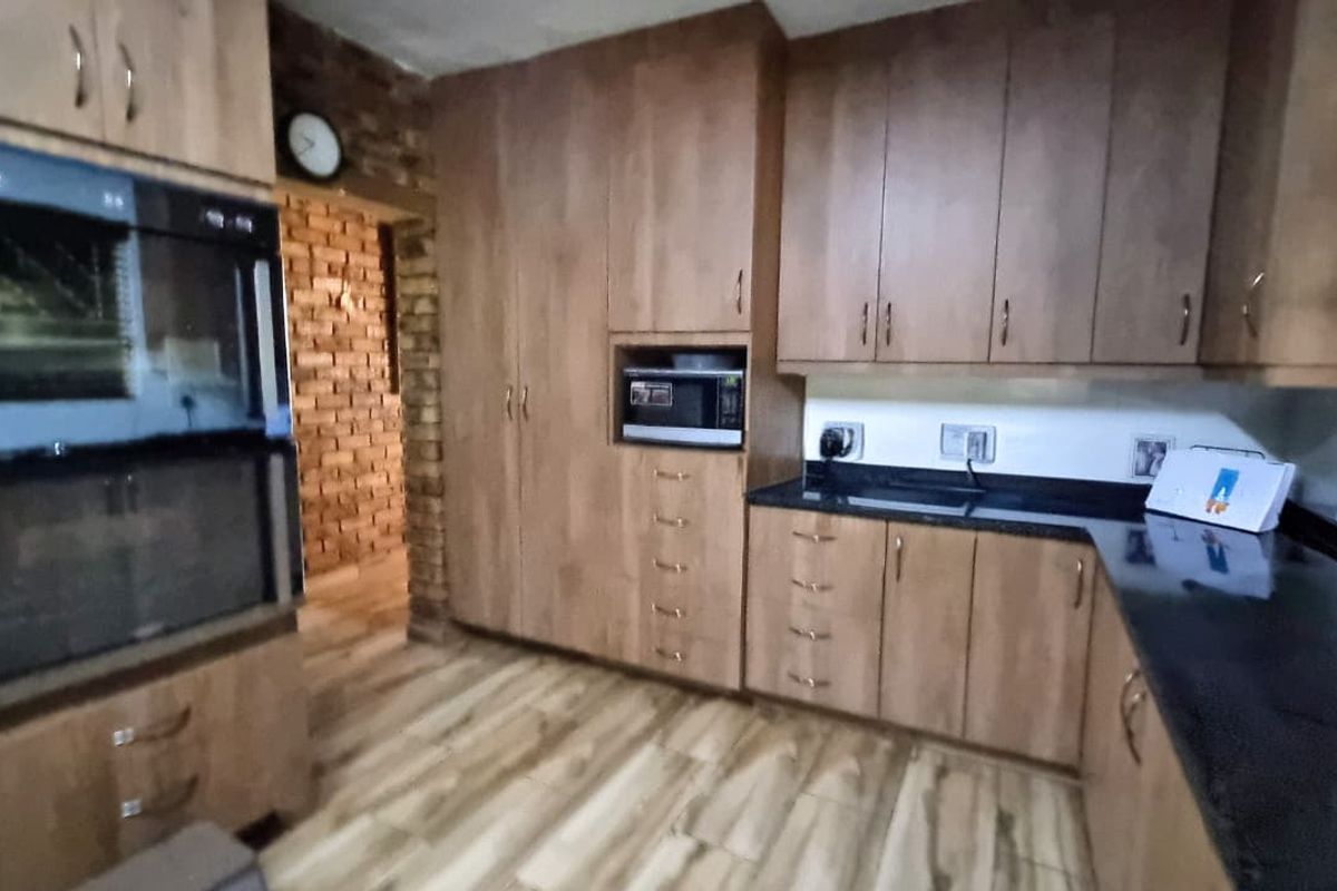 A functional kitchen featuring wood-look cabinetry, dark granite countertops, a built-in double oven, and a microwave nook, with an adjacent exposed brick wall.