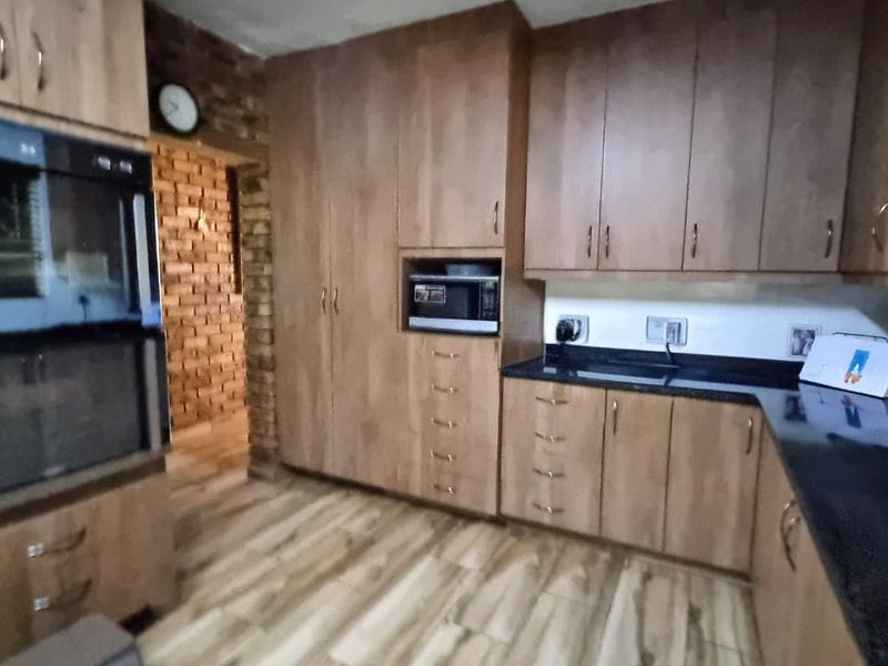 A functional kitchen featuring wood-look cabinetry, dark granite countertops, a built-in double oven, and a microwave nook, with an adjacent exposed brick wall.