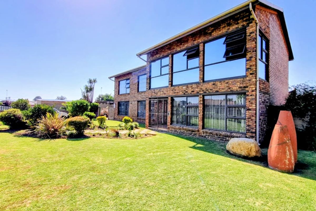 A two-story face-brick residential property featuring large glass windows, a well-maintained lawn, and landscaped garden areas.