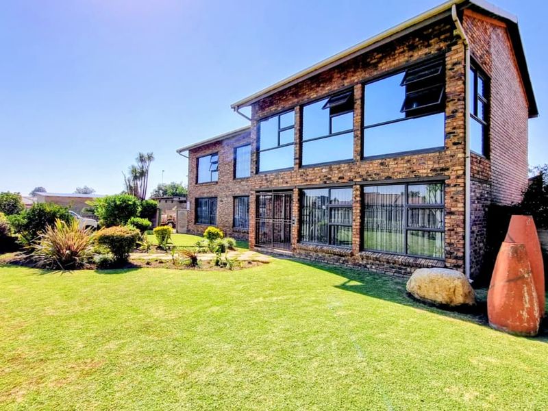 A two-story face-brick residential property featuring large glass windows, a well-maintained lawn, and landscaped garden areas.