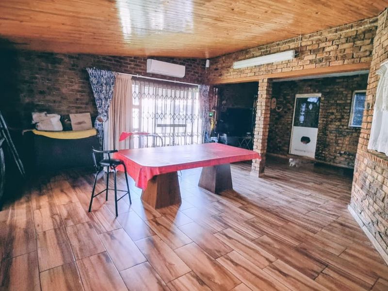 Spacious living area featuring exposed brick walls, wood-look tiled flooring, and a timber-paneled ceiling, equipped with a wall-mounted air conditioning unit.