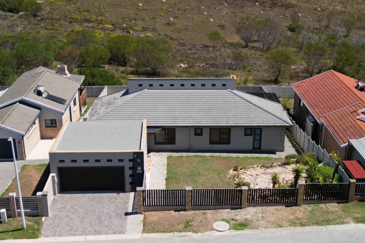 Aerial view of a modern residential property featuring a tiled roof, double garage, paved driveway, and enclosed garden area.