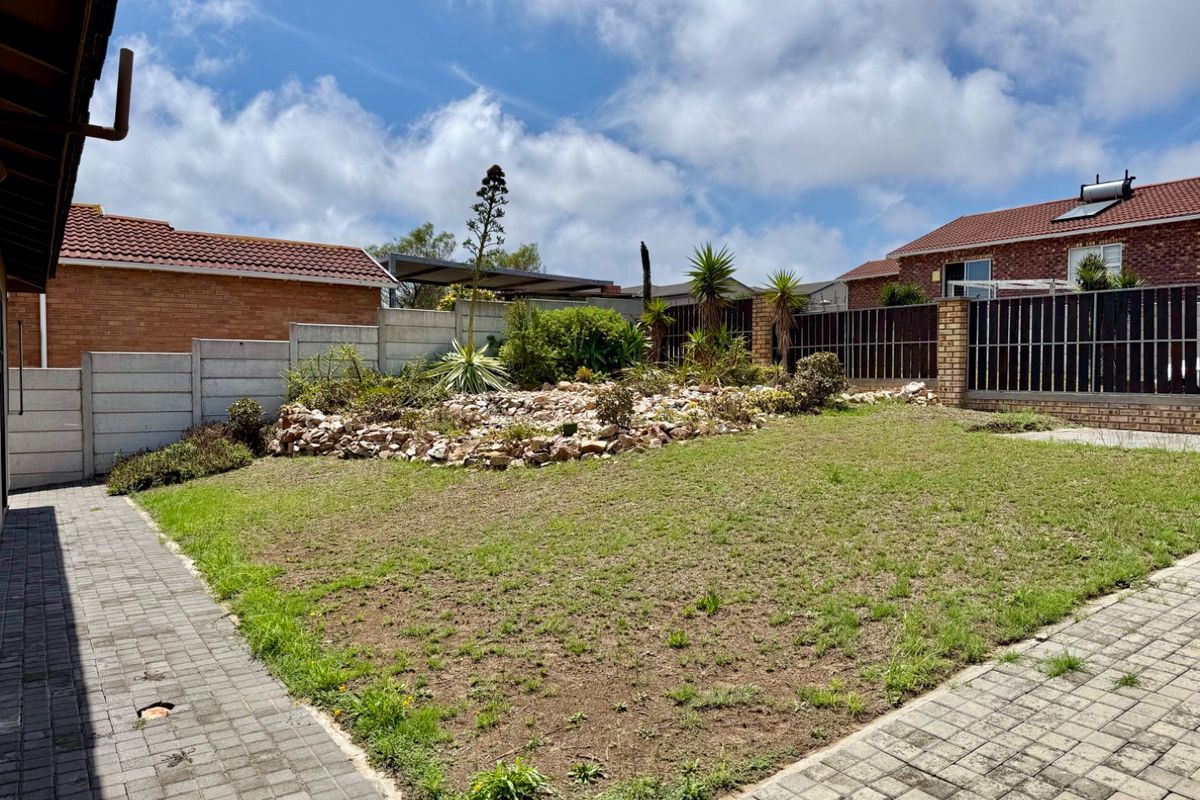 A private rear garden featuring a paved walkway, a central rock garden, and a combination of precast concrete and timber slat boundary fencing.