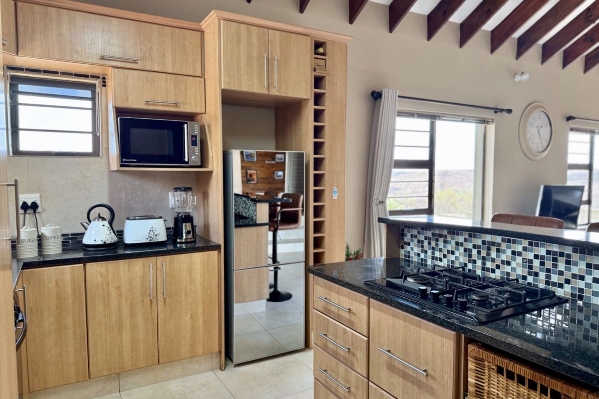 Modern kitchen featuring light wood cabinetry, granite countertops, a gas hob, mosaic backsplash, and exposed timber ceiling beams, offering a warm and functional space.