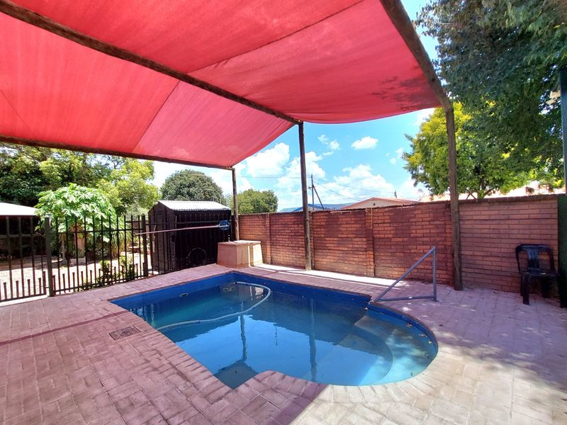 Outdoor pool area featuring a swimming pool with a red shade sail, brick paving, and a brick boundary wall.