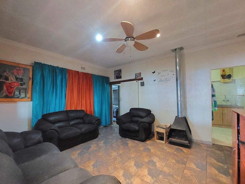 Living room featuring tiled flooring, a ceiling fan, and a freestanding fireplace, with direct access to an adjacent room.