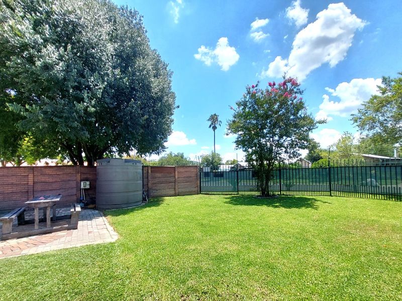 A well-maintained private garden featuring a lush lawn, paved patio area, water storage tank, and secure perimeter fencing.