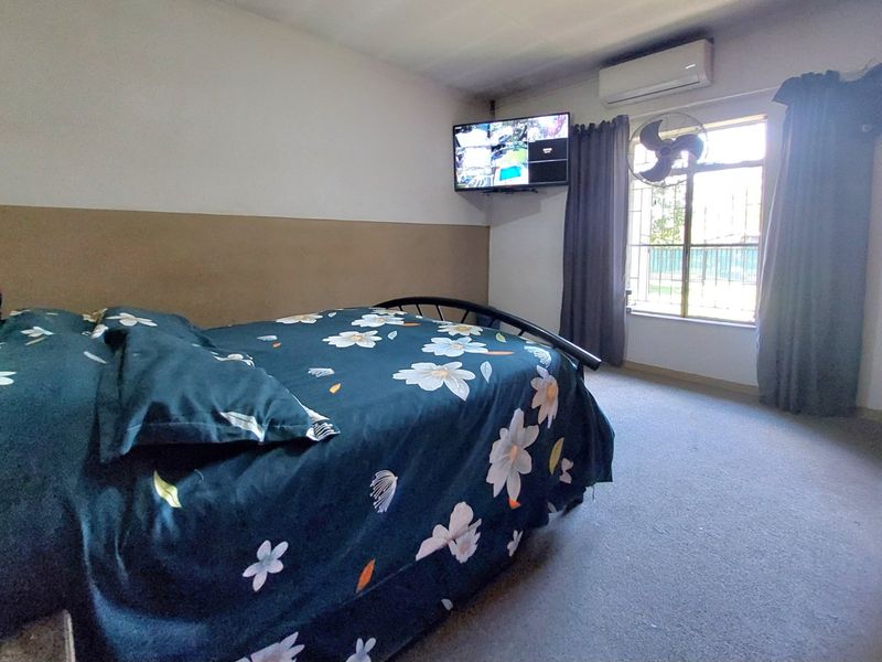 A bedroom featuring a split-system air conditioner, security bars on the window, and wall-mounted television, with carpeted flooring.