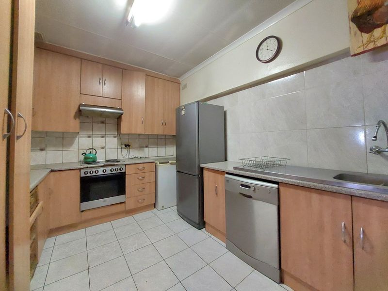 A functional kitchen featuring light wood-tone cabinetry, tiled backsplash, tiled flooring, and integrated appliances, offering a practical layout for daily meal preparation.