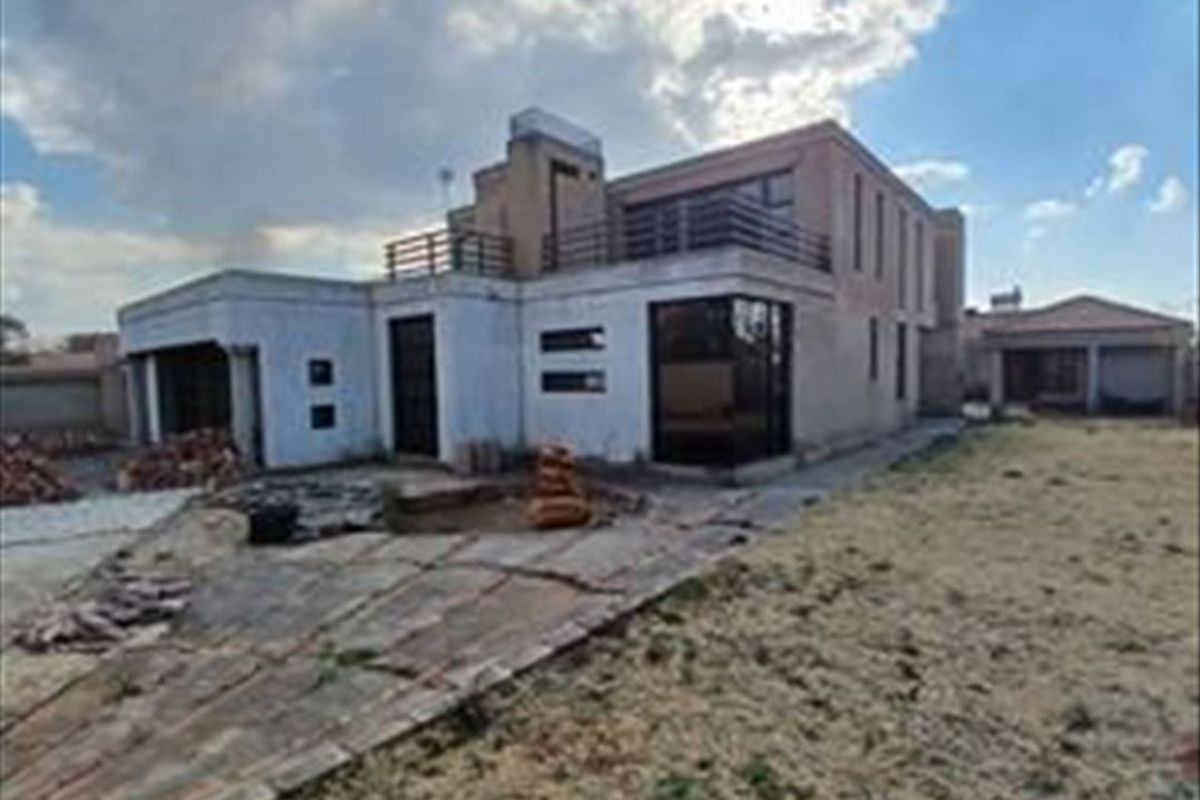 Rear view of a multi-story residential property featuring a balcony, paved patio area, and attached garage, set within a large garden plot.