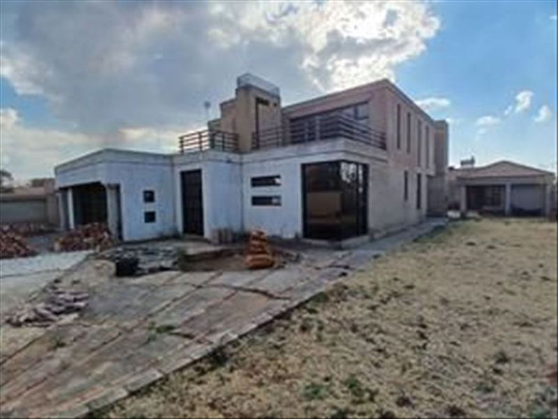 Rear view of a multi-story residential property featuring a balcony, paved patio area, and attached garage, set within a large garden plot.