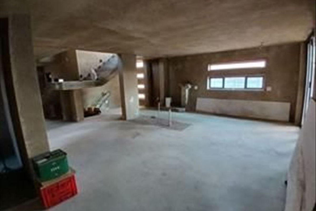 An expansive, unfinished open-plan living area featuring raw concrete walls, flooring, and a structural staircase, offering a blank canvas for renovation.