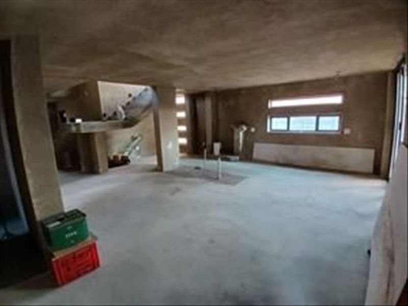 An expansive, unfinished open-plan living area featuring raw concrete walls, flooring, and a structural staircase, offering a blank canvas for renovation.