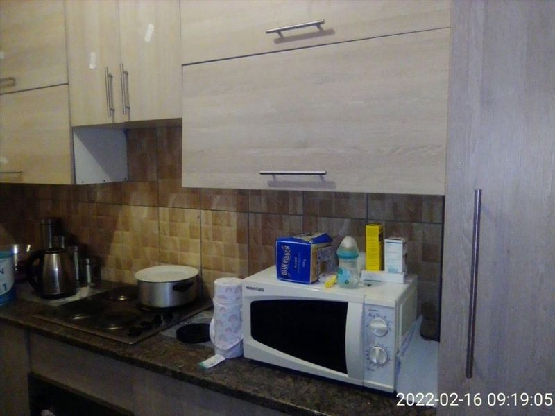 A functional kitchen area featuring light wood-finish cabinetry, a stone countertop, an electric hob, and a tiled backsplash.