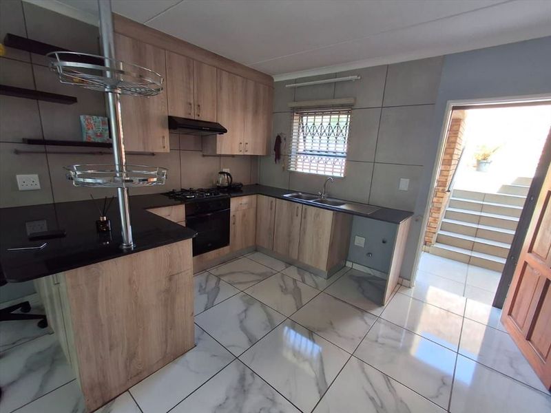 Modern kitchen featuring light wood cabinetry, dark countertops, gas hob, built-in oven, and marble-look tiled flooring with direct access to an outdoor staircase.