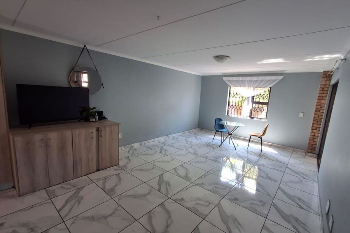 Spacious living area featuring modern marble-look floor tiles, an exposed brick accent pillar, and natural light through a window with security bars.