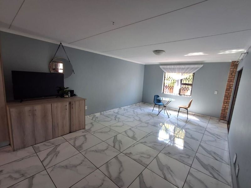 Spacious living area featuring modern marble-look floor tiles, an exposed brick accent pillar, and natural light through a window with security bars.