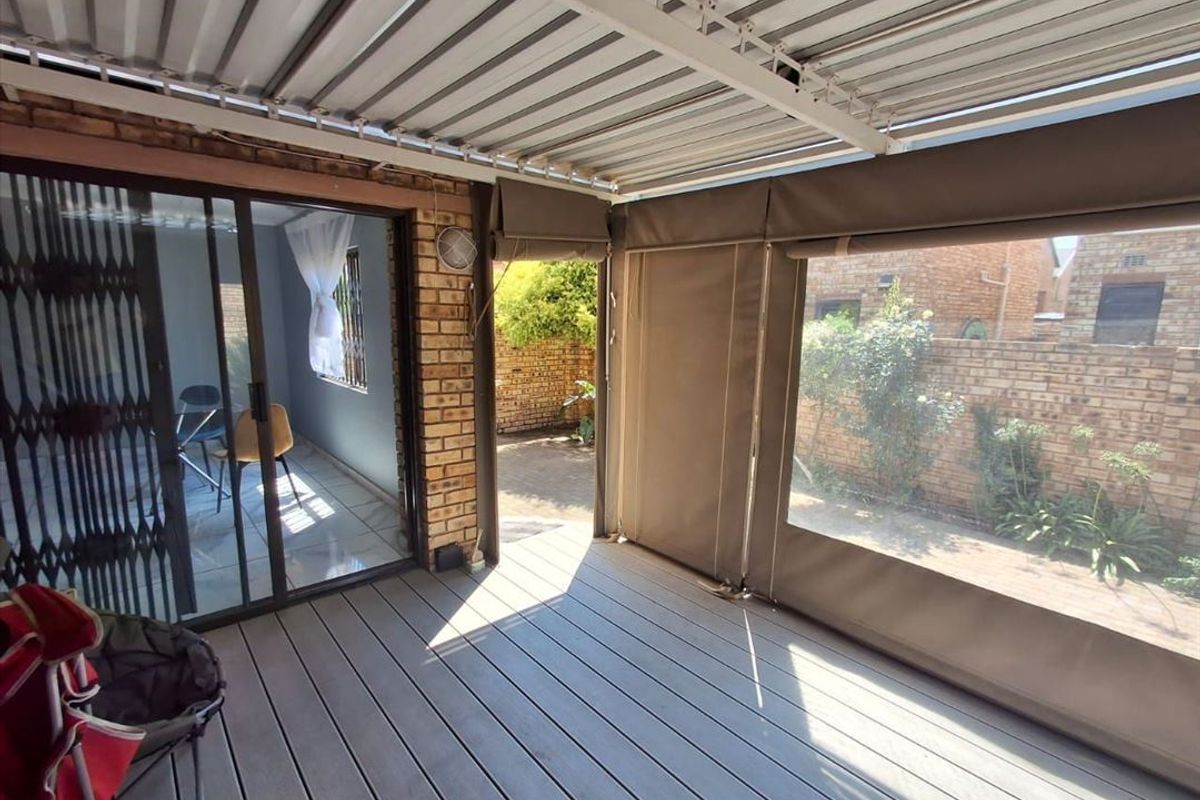 Covered patio area featuring composite decking, roll-up canvas blinds, and direct access to the garden through sliding glass doors.