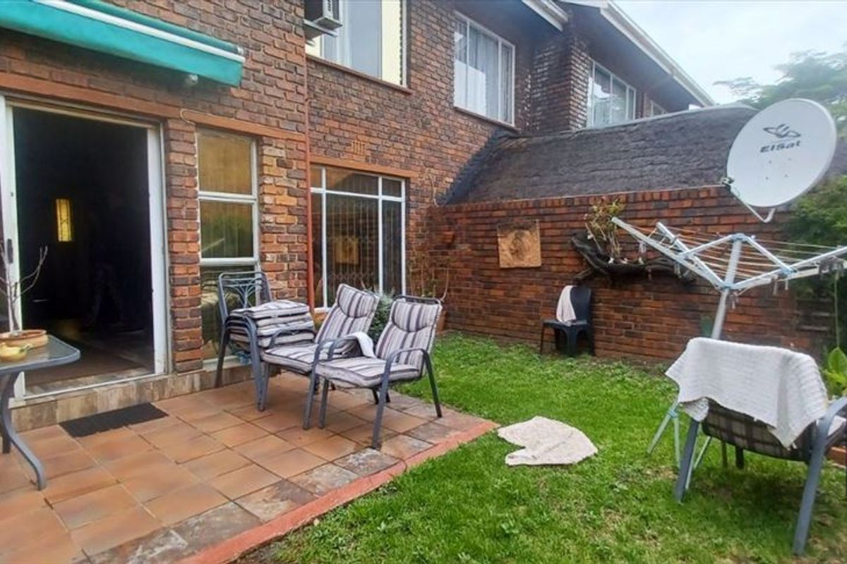 Rear exterior view of a townhouse featuring a brick facade, a tiled patio area, and a small private garden space.