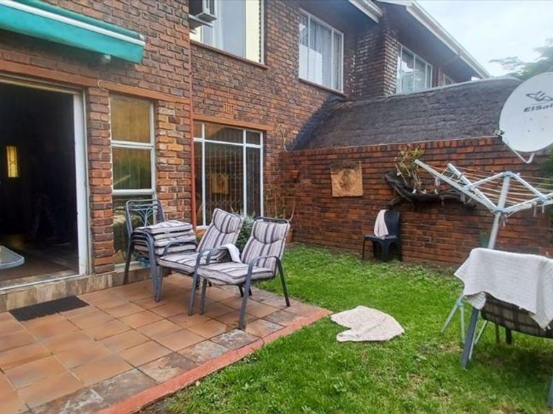 Rear exterior view of a townhouse featuring a brick facade, a tiled patio area, and a small private garden space.