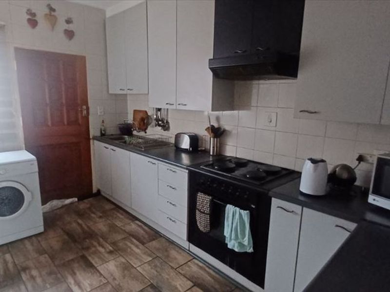 Functional kitchen featuring built-in cabinetry, electric hob, oven, extractor fan, and tiled flooring with space for laundry appliances.