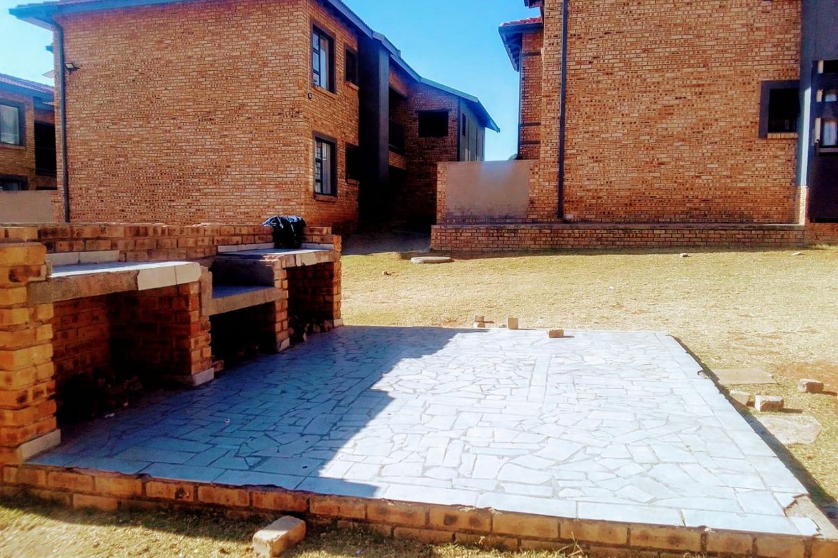 Outdoor communal area featuring a built-in brick braai and paved patio space set between apartment blocks.