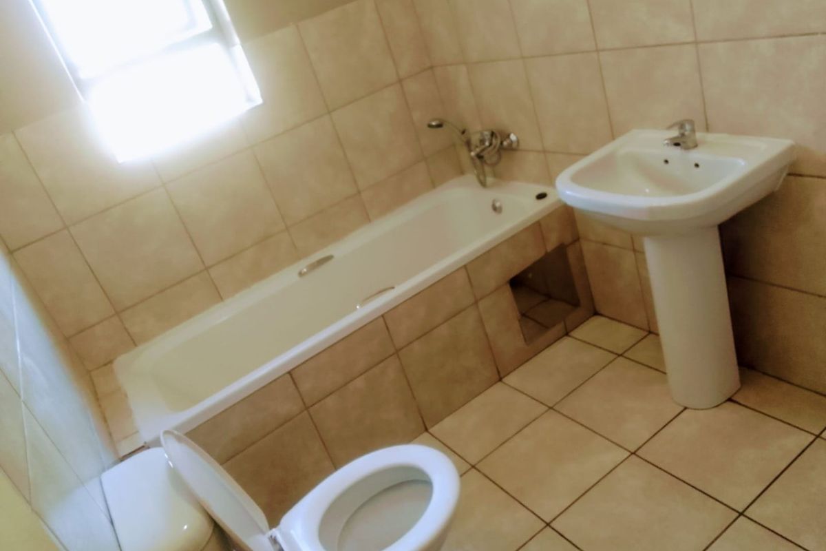 A functional bathroom featuring a standard bathtub, pedestal basin, and toilet with neutral wall and floor tiling.