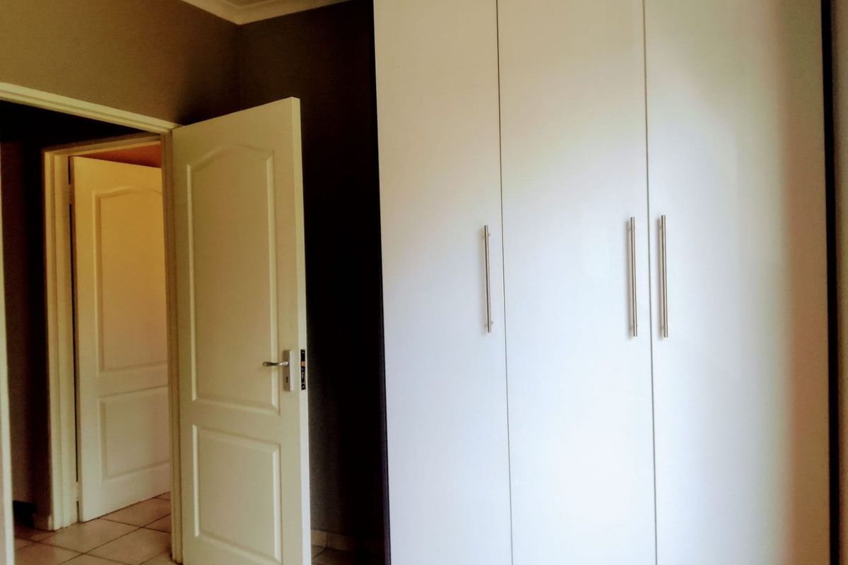 A bedroom featuring built-in cupboards with modern handles and tiled flooring, leading into an adjacent room through an open doorway.