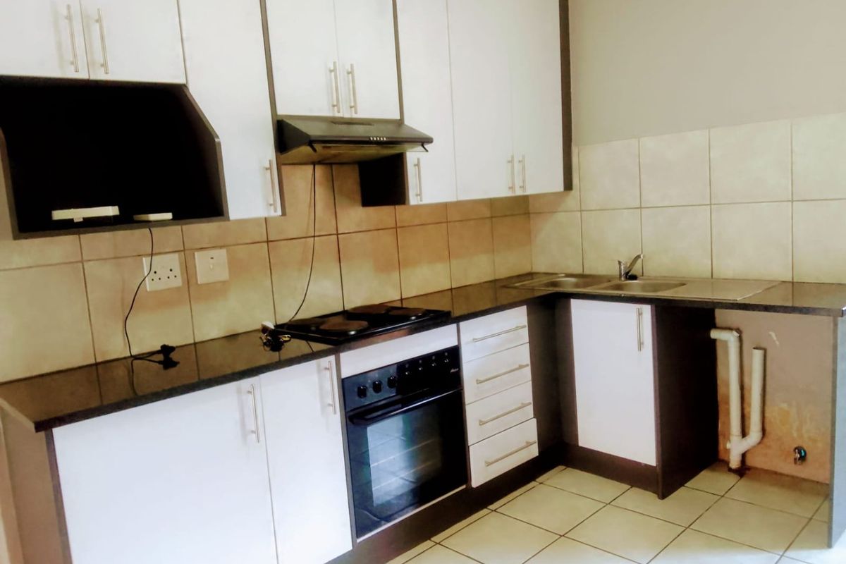A functional kitchen featuring white cabinetry, dark countertops, built-in oven, hob, and extractor fan, with tiled backsplash and flooring.