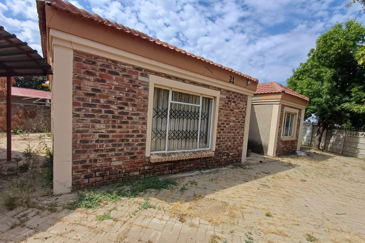 Exterior view of a brick-faced house featuring security bars on windows, a tiled roof, and an adjacent paved yard area.