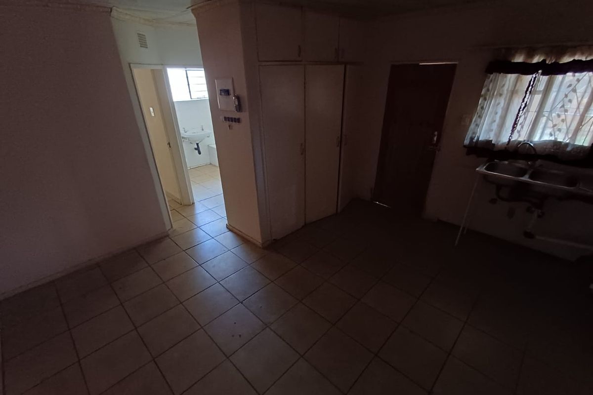 A dated kitchen area featuring tiled flooring, built-in cabinetry, and a double sink, with an adjacent doorway leading to a bathroom.