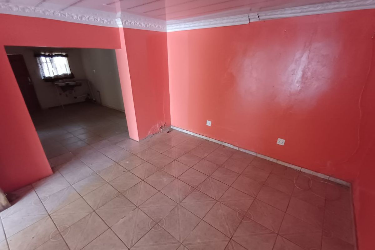 An empty living area featuring tiled flooring, bright orange walls, and decorative ceiling cornices, with an adjacent room visible through the opening.