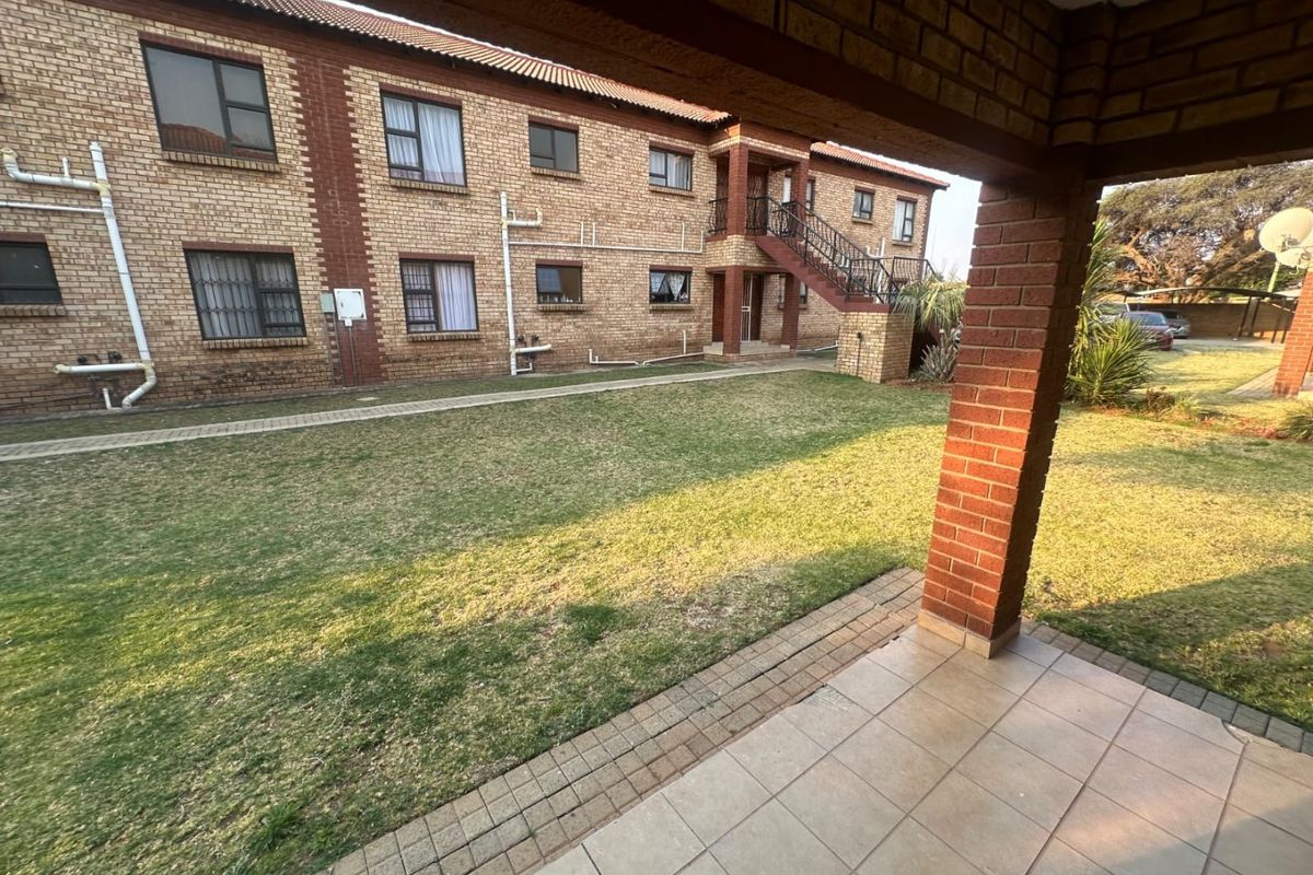 View of the apartment complex exterior featuring a tiled patio, communal lawn, and brick facade with external staircase access.
