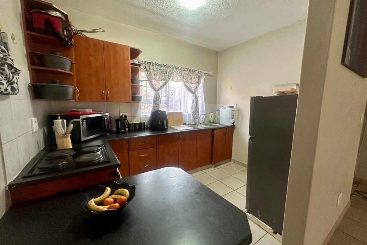 A functional kitchen featuring laminate cabinetry, dark countertops, an electric hob, and tiled flooring, offering a practical layout for daily meal preparation.