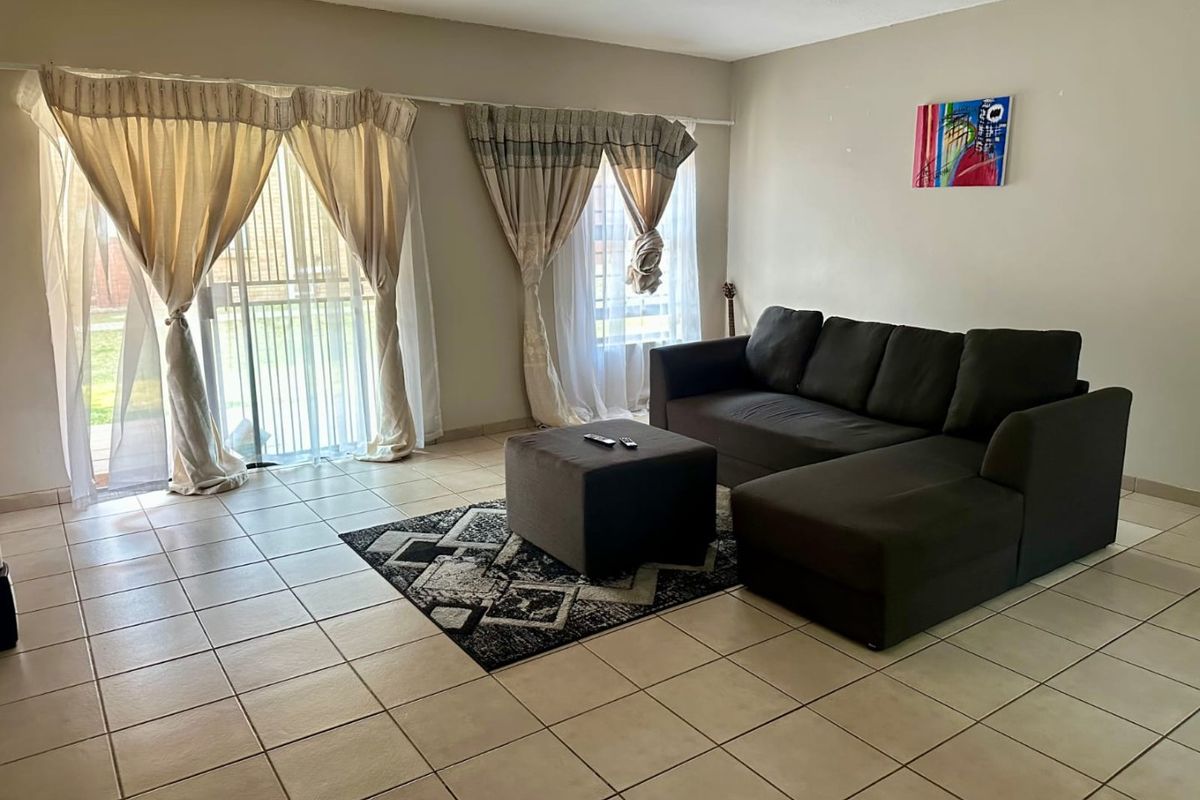 A spacious living room featuring neutral tiled flooring and large sliding glass doors that provide natural light and access to the exterior.