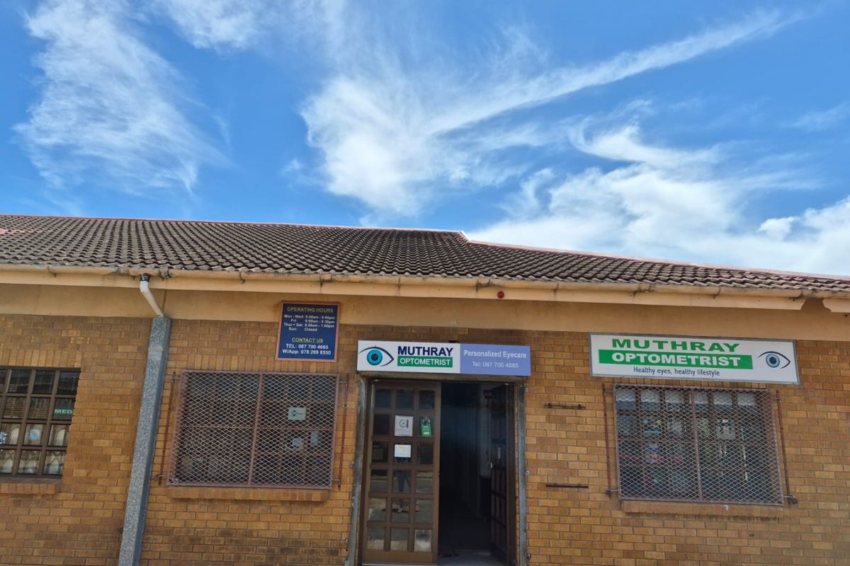 Front facade of a commercial optometrist practice featuring face-brick construction, tiled roofing, and security-grille protected windows.