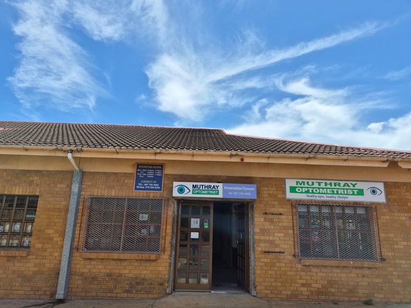 Front facade of a commercial optometrist practice featuring face-brick construction, tiled roofing, and security-grille protected windows.