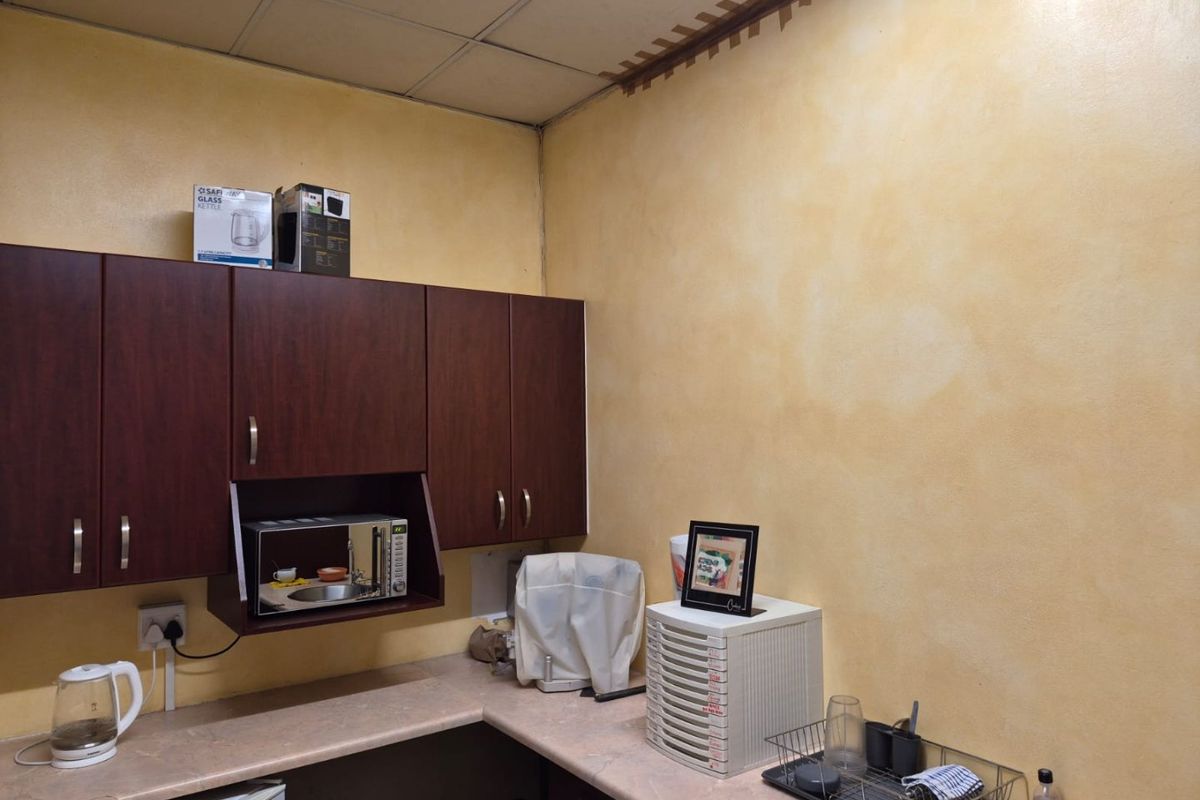 A compact kitchen area featuring dark wood-finish cabinetry, laminate countertops, and a built-in microwave, requiring cosmetic updates to the walls and ceiling.