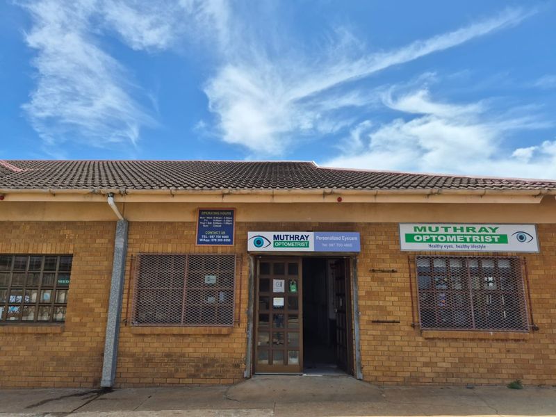 Front facade of a commercial optometrist practice featuring brick construction, tiled roofing, and prominent business signage with security grilles on windows.