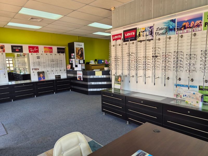 Commercial retail space configured as an optometry practice, featuring extensive wall-mounted eyewear display shelving, built-in storage cabinetry, and a central reception counter.