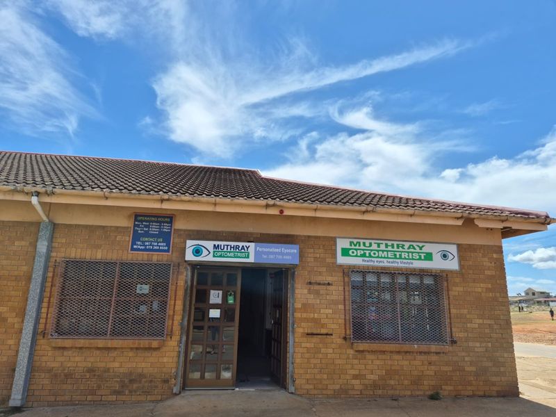 Front facade of a commercial optometrist practice featuring brick construction, tiled roofing, and prominent business signage with security grilles on windows.