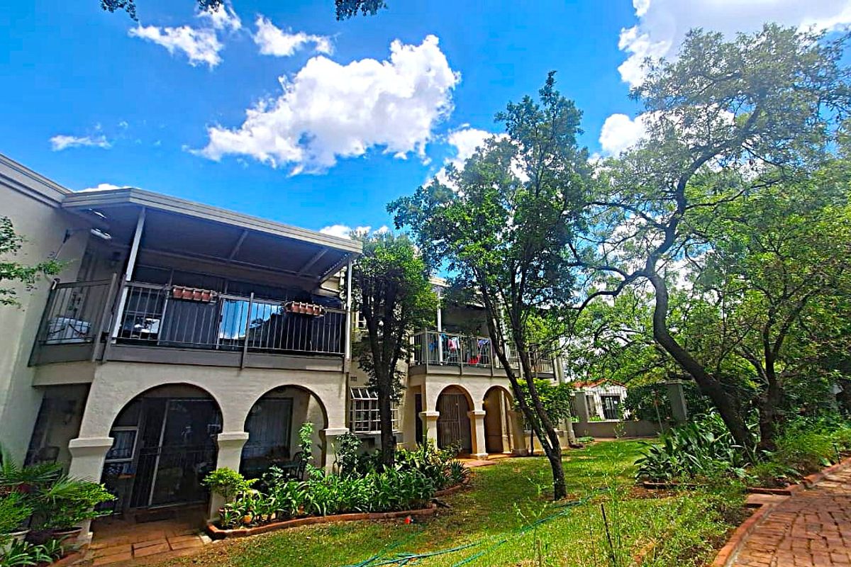 Rear view of the townhouse featuring a covered patio, upper-level balcony with metal railings, arched architectural details, and a lush garden with brick pathways.