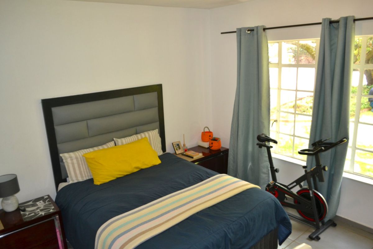 A functional bedroom featuring tiled flooring and a window with security bars, providing natural light and a view of the exterior.