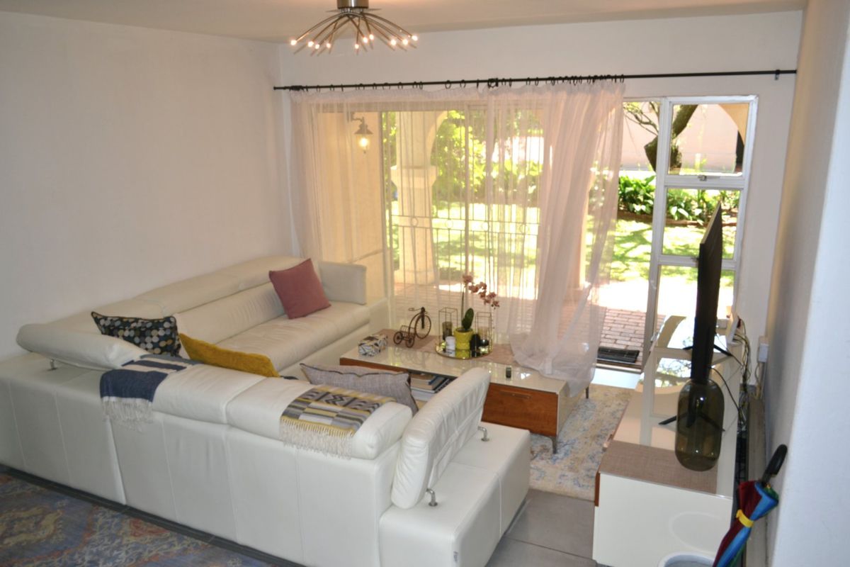 A bright living room featuring tiled flooring and a large sliding glass door that provides direct access to the outdoor patio and garden area.