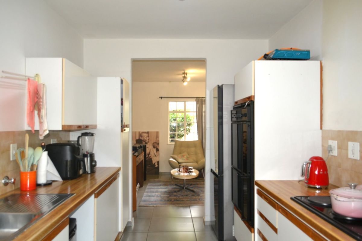 A functional galley-style kitchen featuring white cabinetry, wood-look laminate countertops, a built-in double oven, and tiled flooring, leading into an adjacent living area.