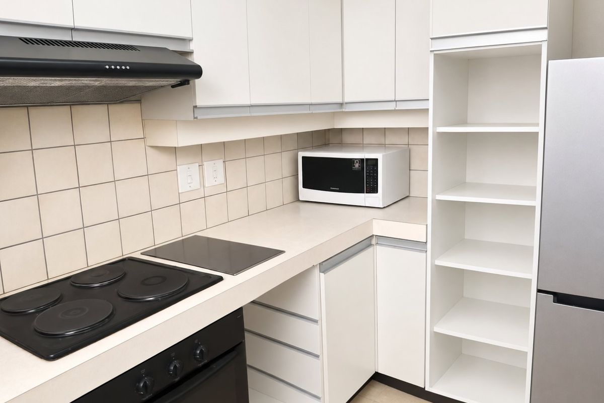 A functional kitchen featuring white cabinetry, a tiled backsplash, an electric hob with an extractor fan, and integrated open shelving for storage.