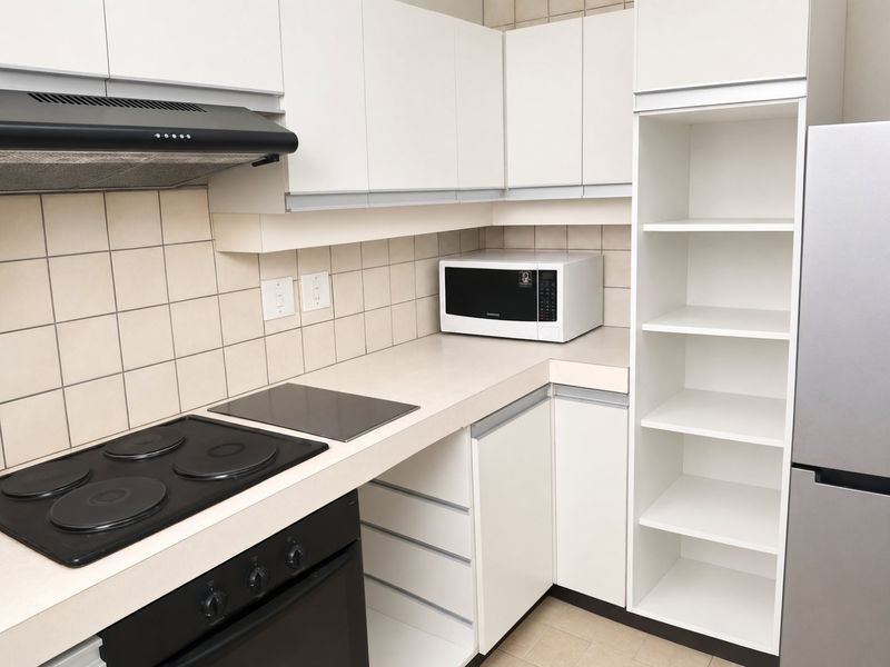 A functional kitchen featuring white cabinetry, a tiled backsplash, an electric hob with an extractor fan, and integrated open shelving for storage.